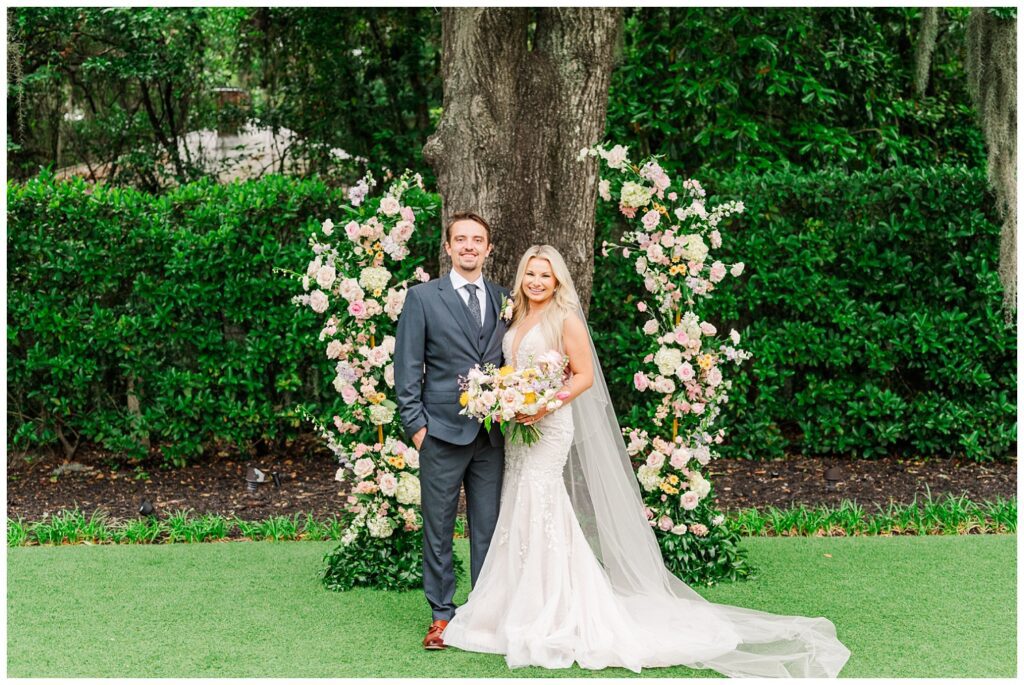 wedding couple posing in front of a large tree and floral decorations