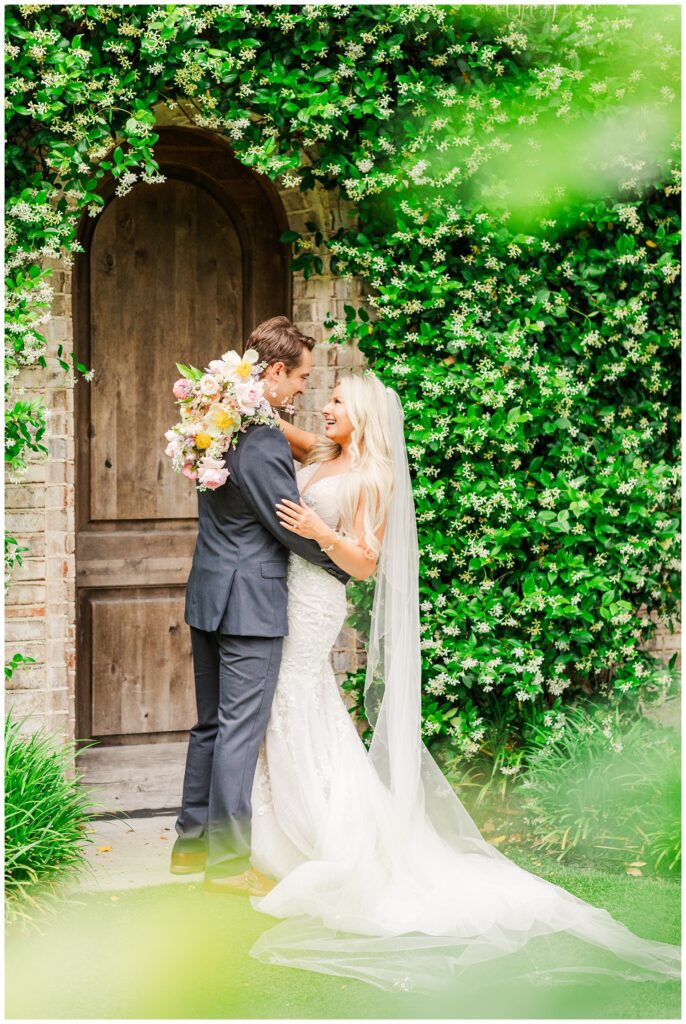 wedding couple posing in front of a wooden door and white floral bushes