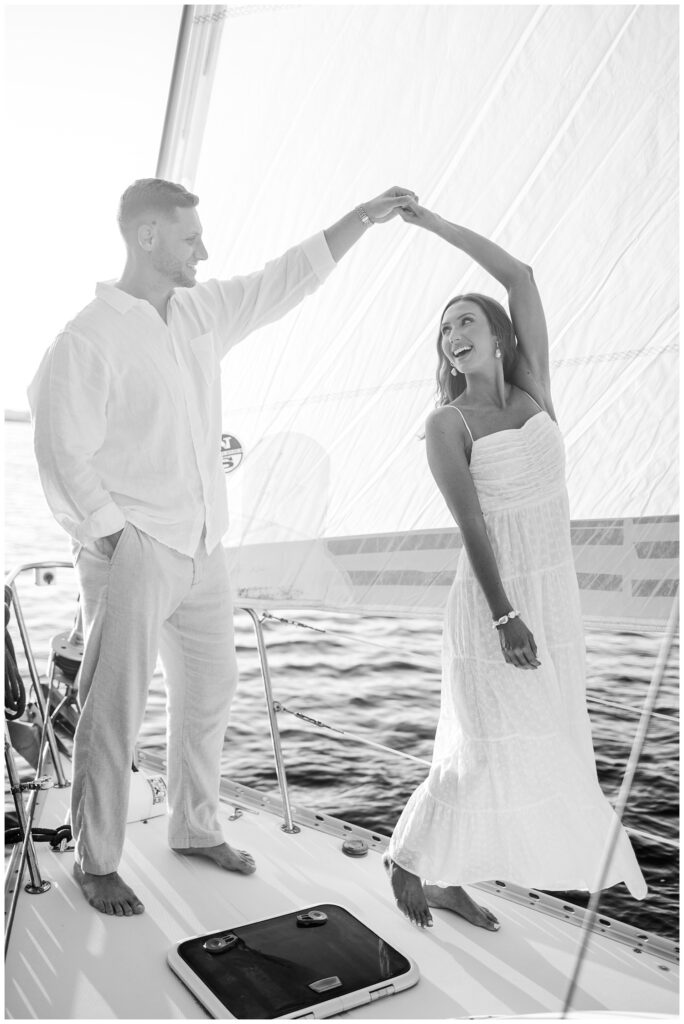 couple dancing together in front of a white sails on a boat at golden hour 