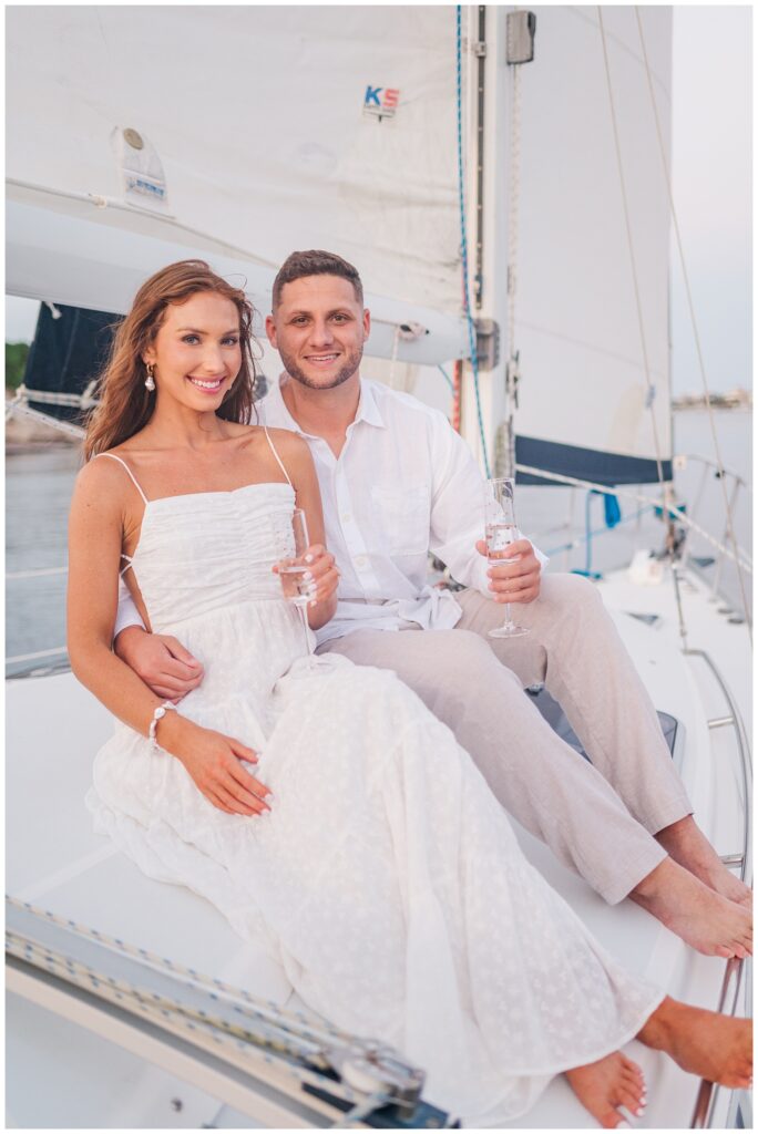 engaged couple holding champagne glasses on a sailboat in Carolina Beach