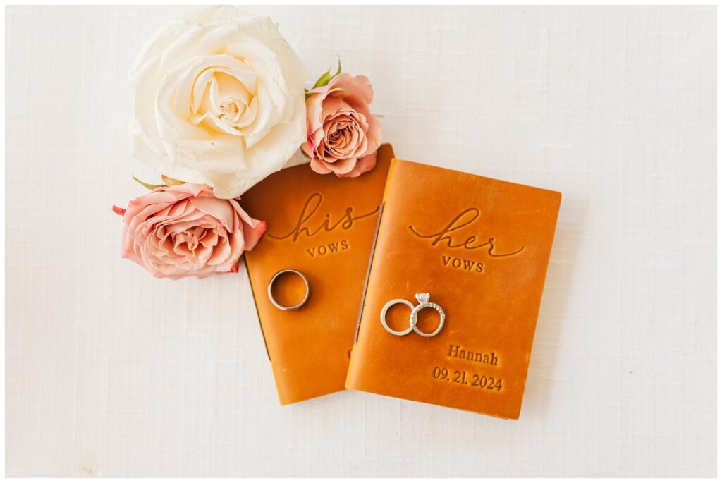 wedding rings sitting on top of brown vow books next to white and pink blooms