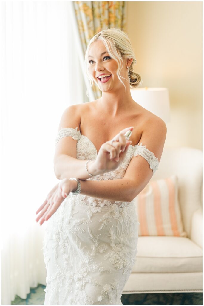 bride spraying on perfume after getting dressed in a lace wedding gown