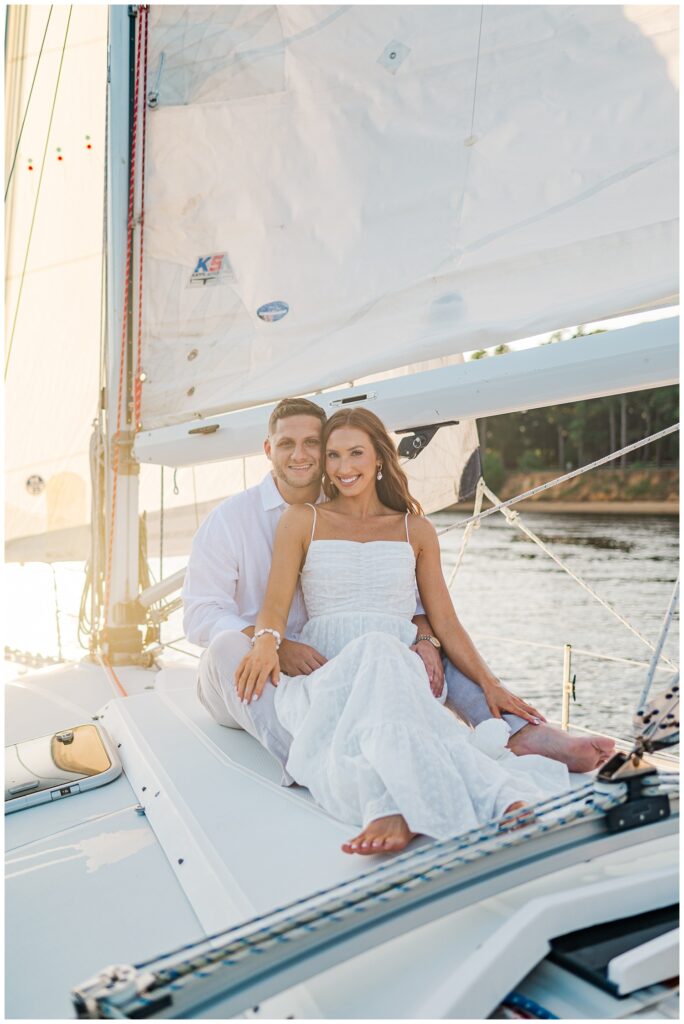 girl sitting in guy's lap for engagement session on a sailboat in NC