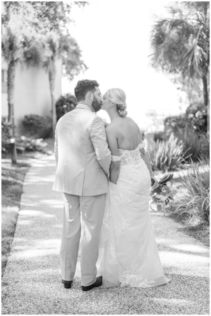 groom and bride share a kiss while walking along the sidewalk at Sea Pines Resort