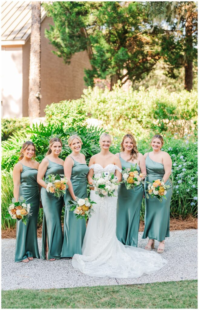 bridal party posing on the sidewalk wearing dark green sage dresses 