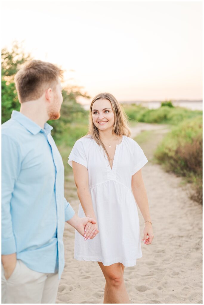 man looking back at his fiancee on the beach for Fort Fisher engagement portraits 