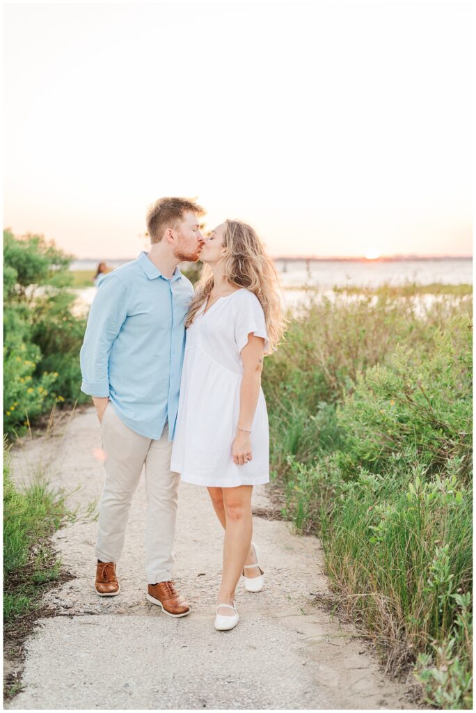 engagement couple pause for a kiss along a sandy beach path at Fort Fisher