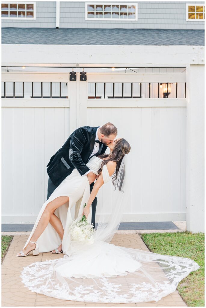 groom dips back the bride for a kiss in front of the venue outside 