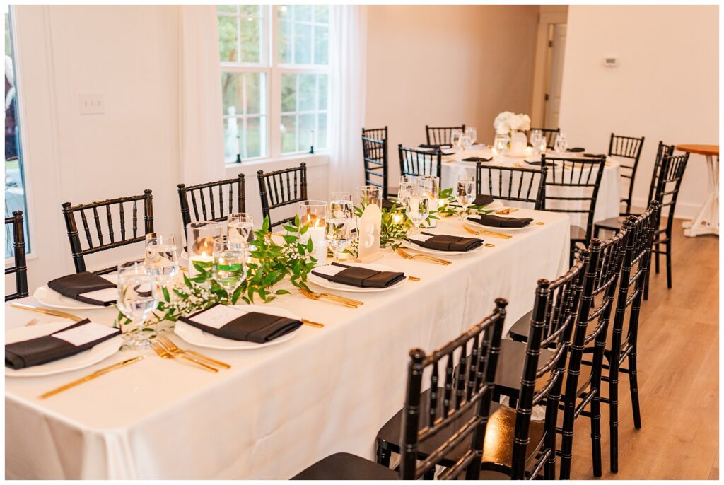 long reception table with black chairs and with candles and greenery decorations