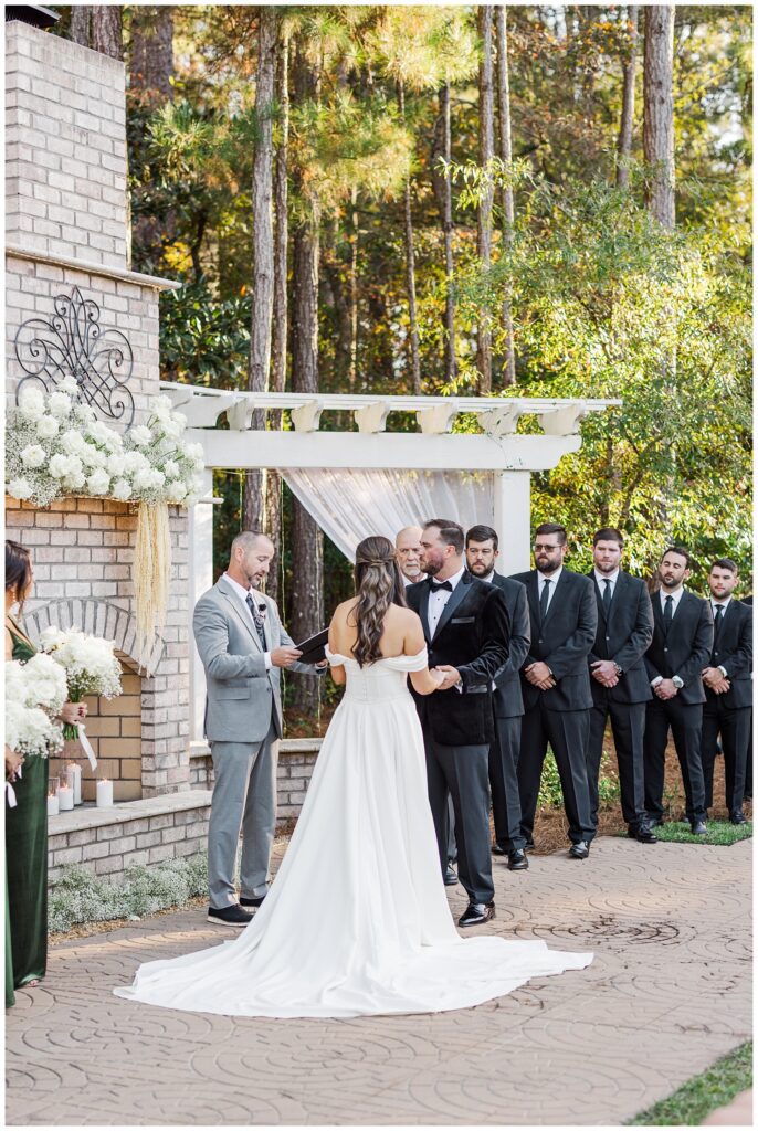 bride and groom standing at the altar holding hands while the groomsmen look on