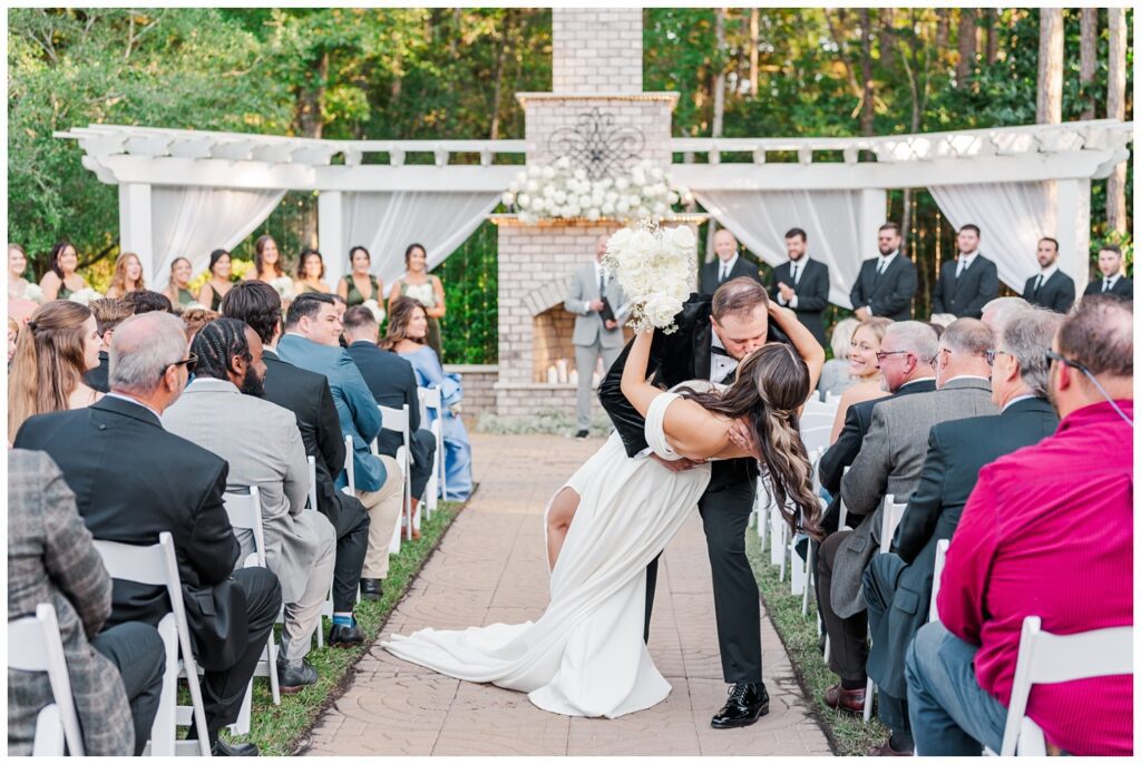 groom dips bride back for a kiss in the center of the aisle