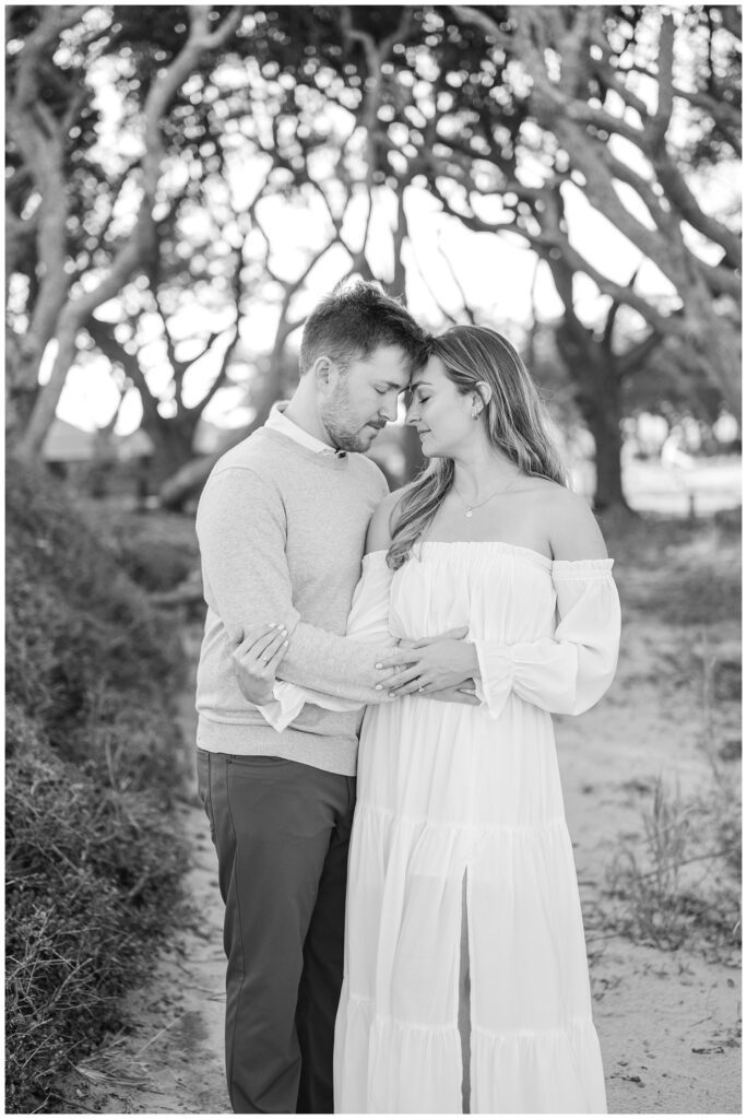 couple touching foreheads on the sand in front of live oaks at Fort Fisher