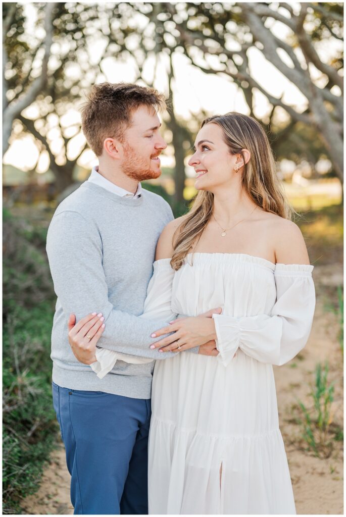 couple smiling at each other while posing on the sand at Fort Fisher, NC