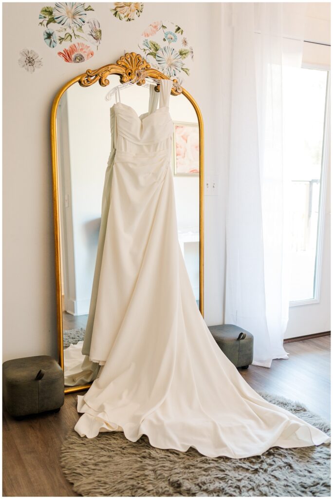 off white wedding dress hanging from a gold mirror at NC venue