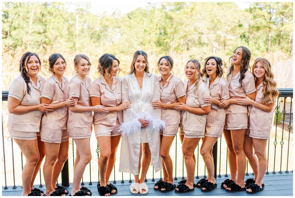 bride with bridesmaids posing together in pink and white pajamas on a balcony