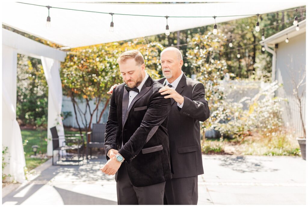 groom's dad helping him adjust his jacket outside at Currie, NC wedding venue