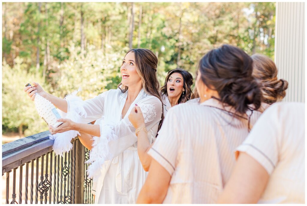 bride popping a hand painted champagne bottle on the balcony with her bridesmaids 