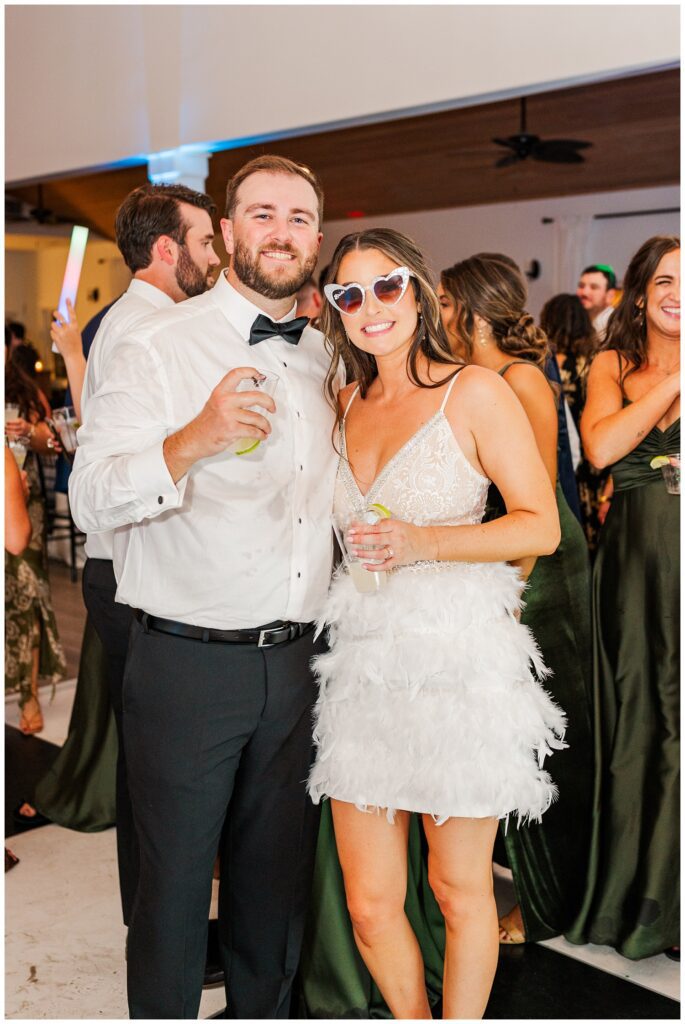 bride wearing a feather party dress and sunglasses posing with the groom at reception