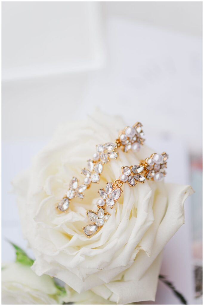 bride's gold and pearl earrings sitting on top of a white rose 