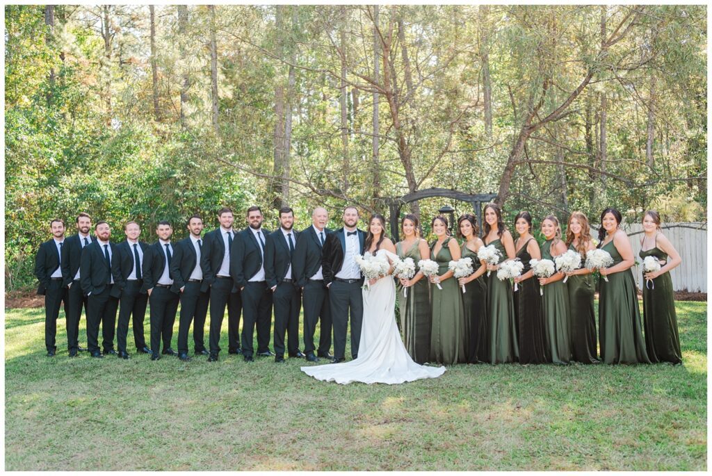 full wedding party posing on the grass with the guys on the left and the girls on the right 