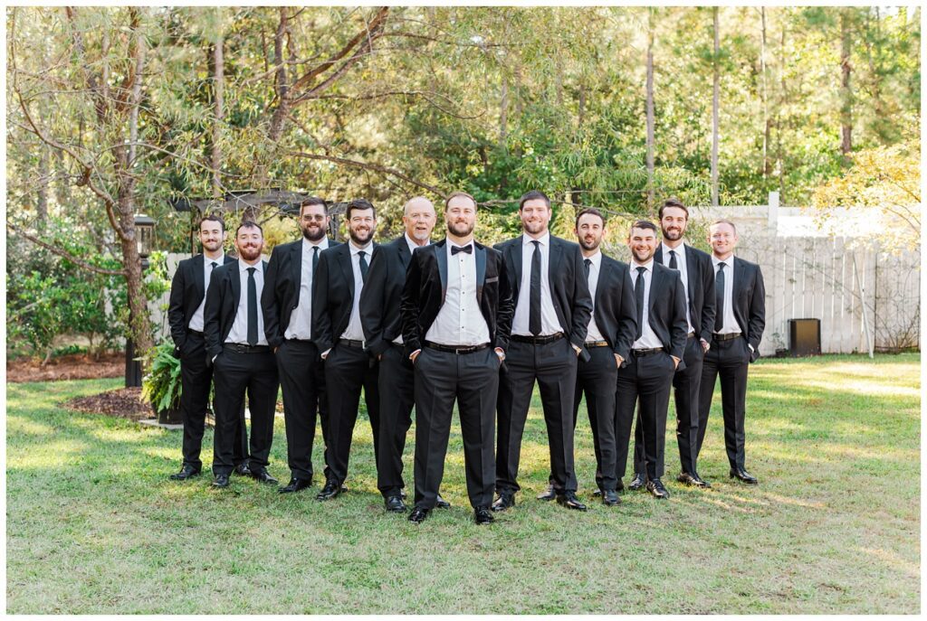 groomsmen posing in a flying V on the grass outside at the wedding venue