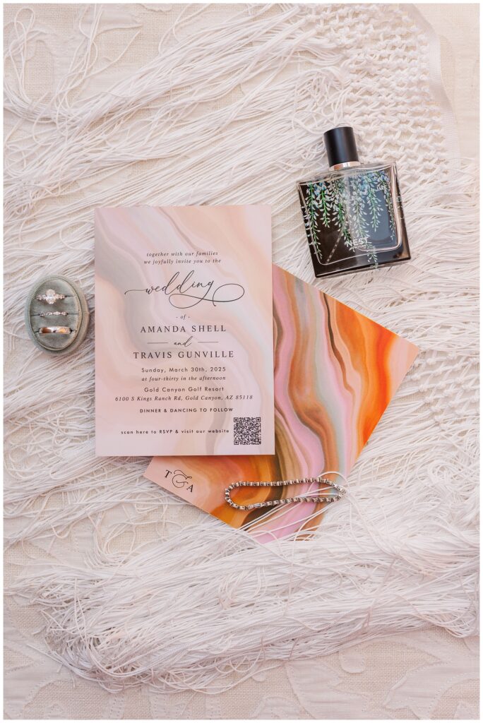 wedding invitation, perfume, wedding rings, and bracelet sitting on the bride's fringe veil