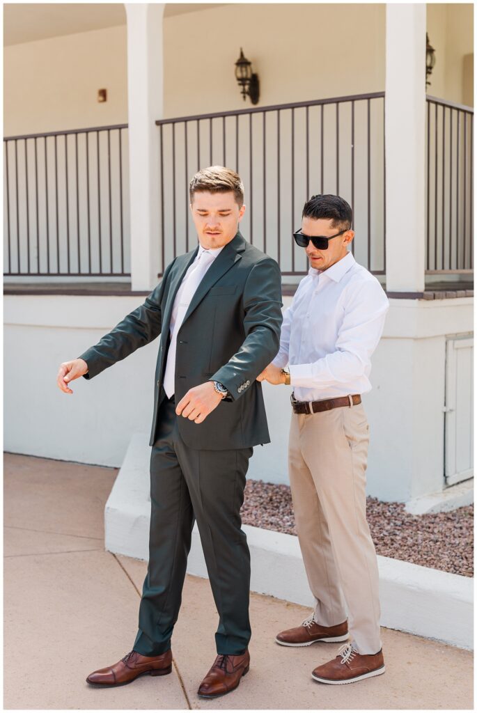 groom's best man helping the groom adjust his jacket next to the porch outside 