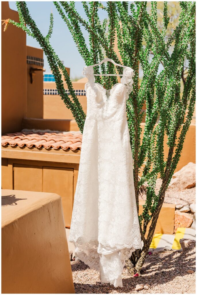 bride's lace wedding dress hanging from a tree outside of the venue 