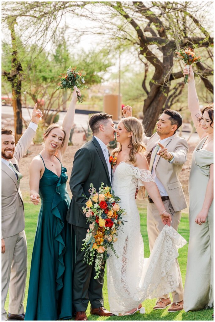 bride and groom share a kiss while the wedding party cheers for them 