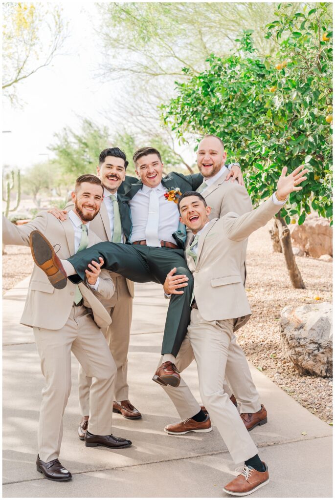 groomsmen holding up the groom on the sidewalk next to the wedding venue in Arizona