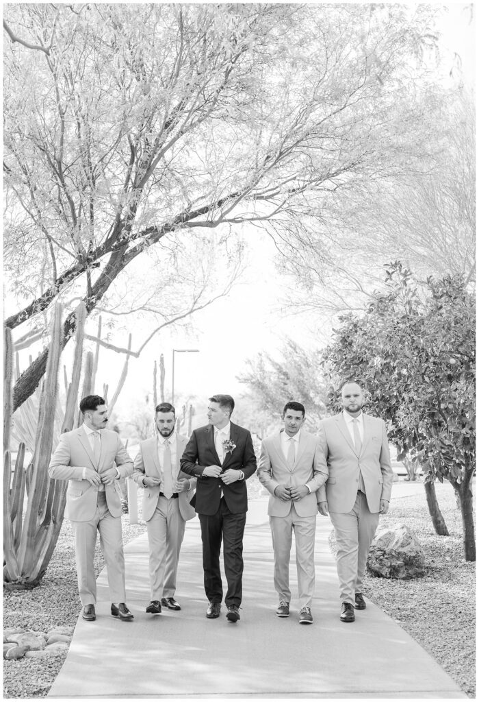 groomsmen walking together adjusting their jackets on the sidewalk next to the wedding venue in Arizona