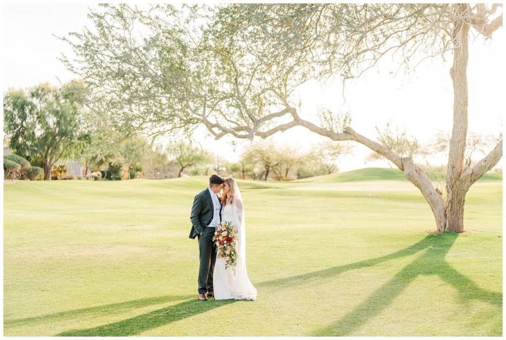 wedding couple posing on the golf course in front of a large tree at venue