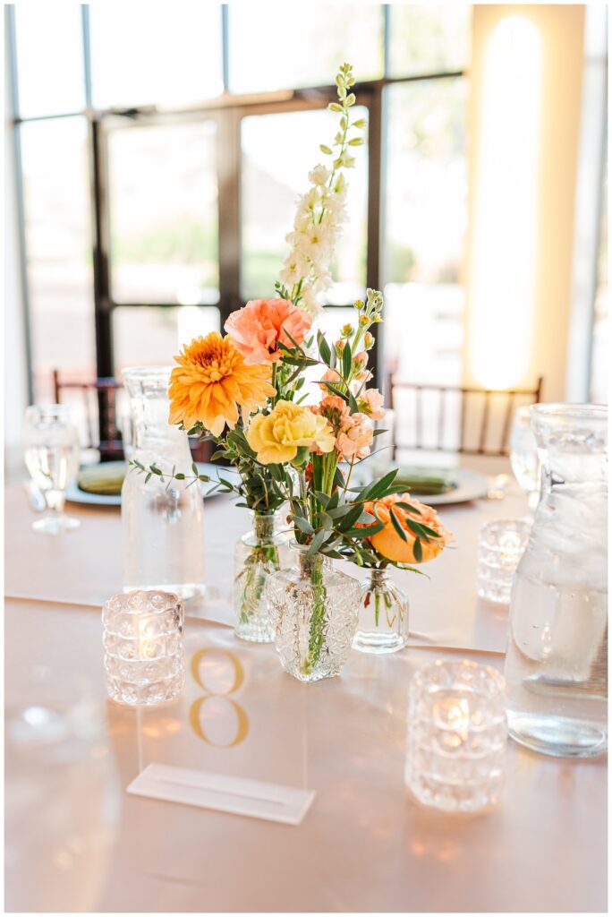 spring reception table details with clear vases of orange and pink flowers