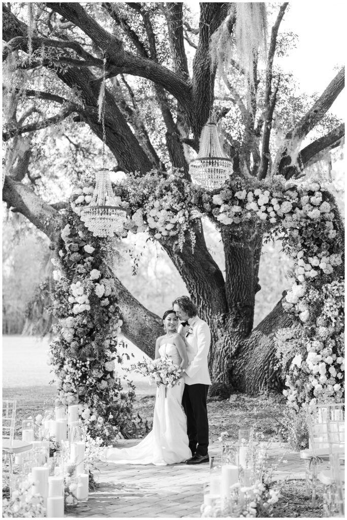 groom standing behind the bride while she holds a large bouquet in front of a live oak