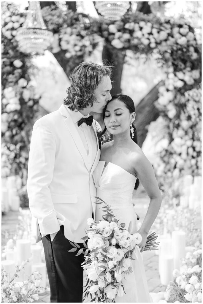 groom kissing the top of the bride's head while she holds her large wedding bouquet