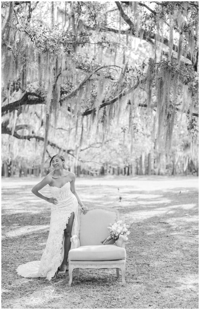 bride holding onto the back of a chair and laughing underneath a live oak tree