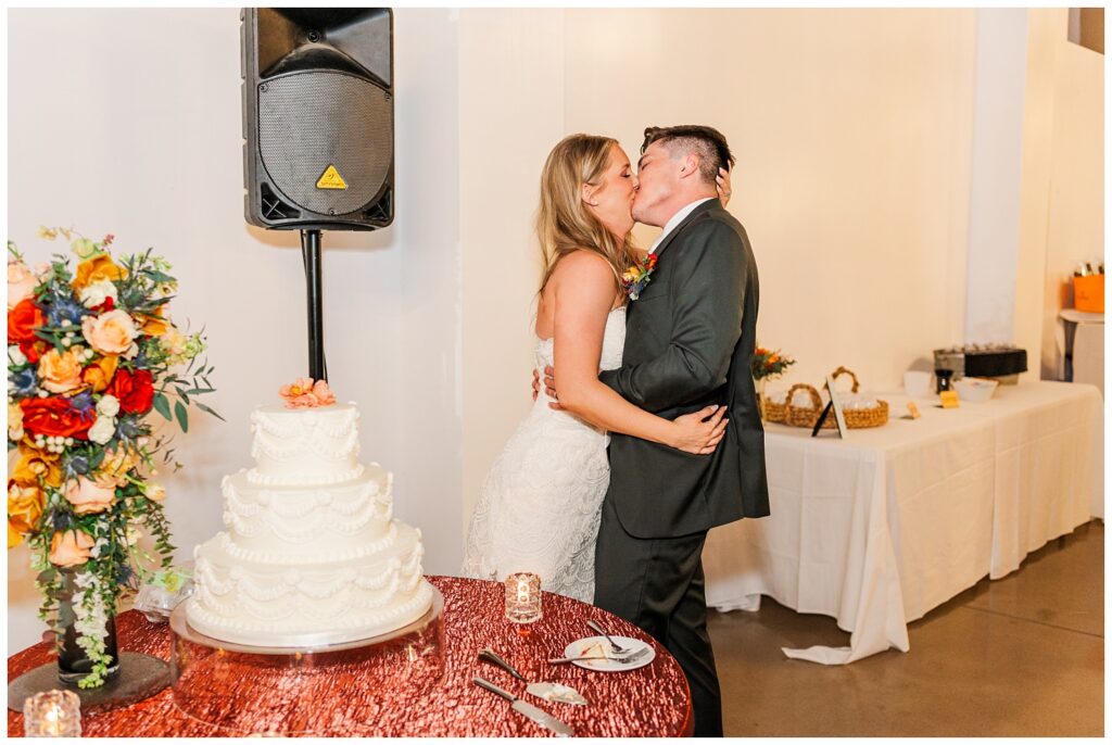bride and groom kiss after cutting the cake at the wedding reception