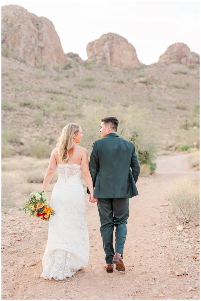 groom and the bride walking together on a trail in Arizona while she holds her bouquet