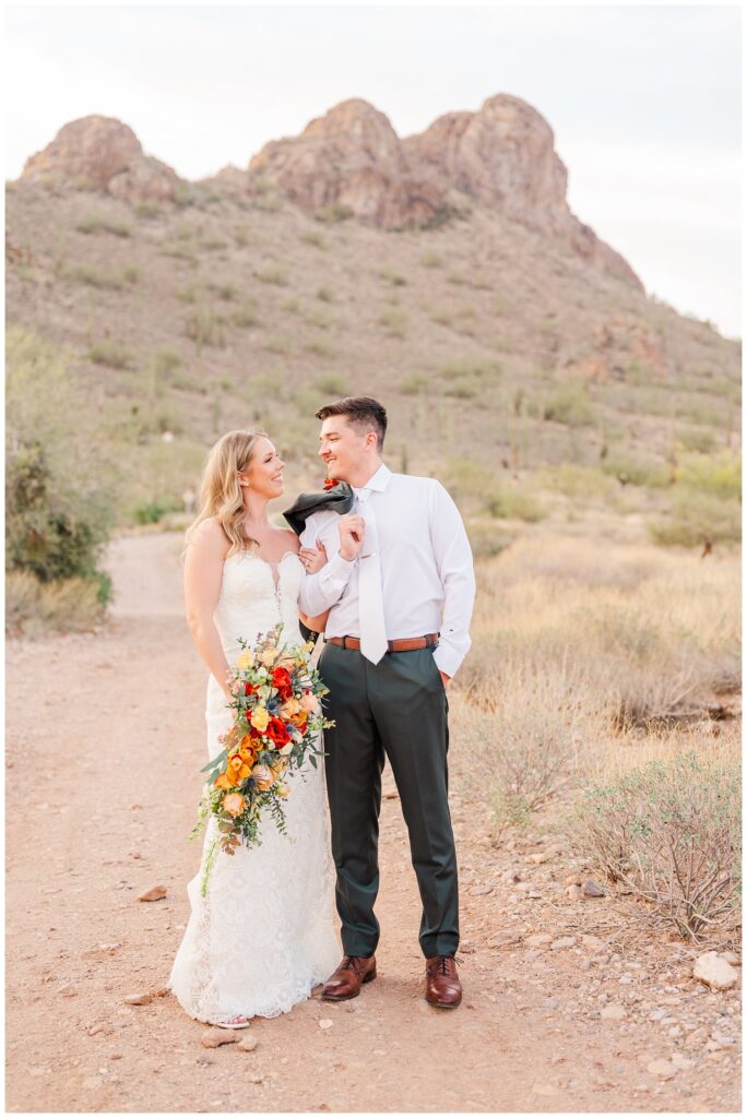 groom holding his jacket over his shoulder and posing with the bride on a trail