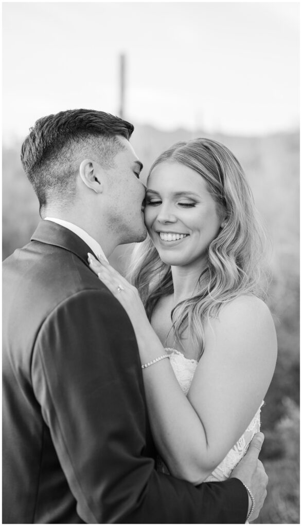 groom kissing the bride on the cheek and posing in the desert
