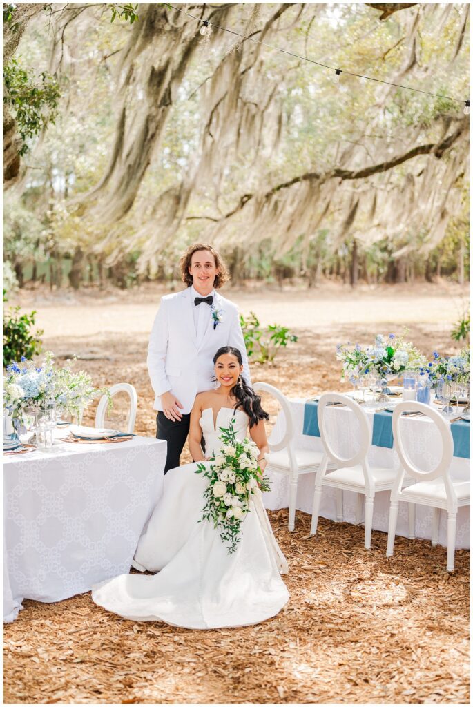 wedding couple sitting in reception chairs outside at the white covered tables 