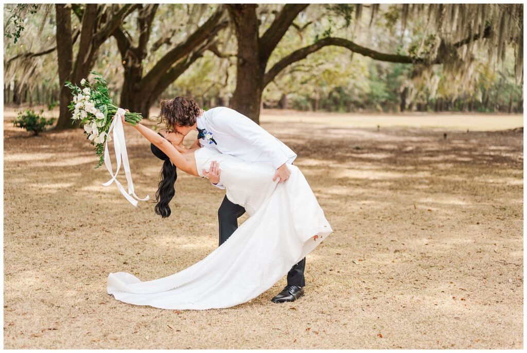 groom dipping the bride back for a kiss as she throws her bouquet in the air at Hewitt Oaks venue