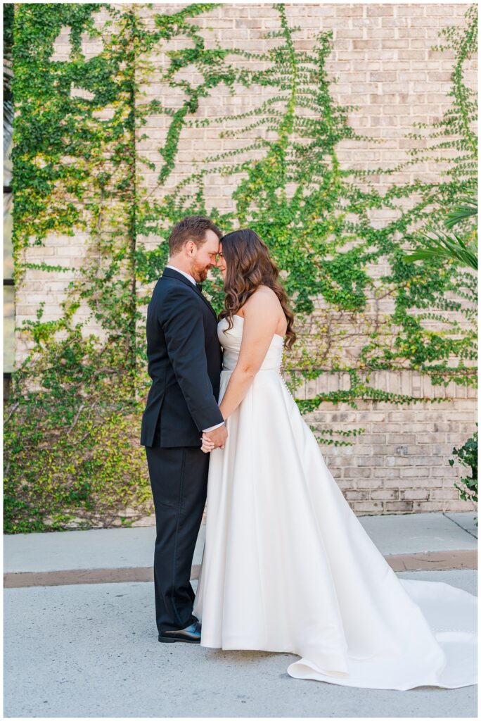wedding couple holding hands and touching foreheads outside the venue in Wilmington