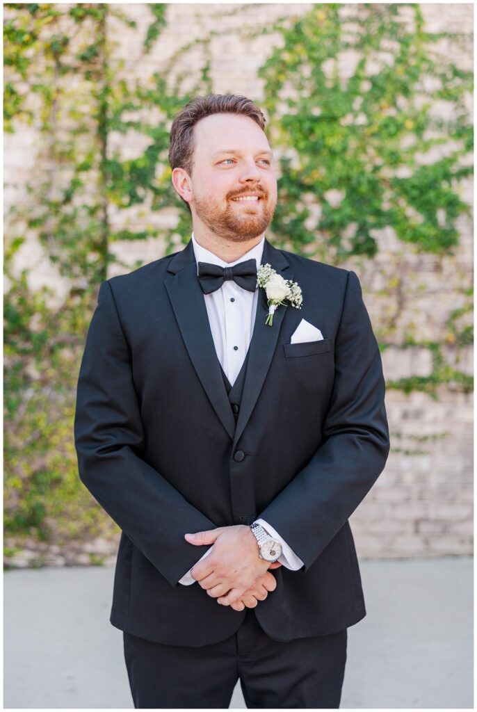 groom looking over to the side while clasping his hands together outside 
