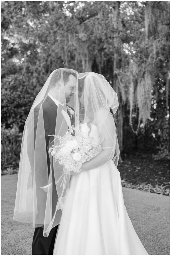 bride and groom posing under the bride's veil outside during cocktail hour