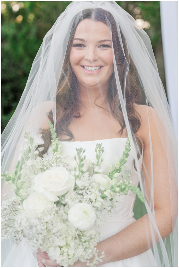 bride holding her bouquet and smiling under the veil after the ceremony
