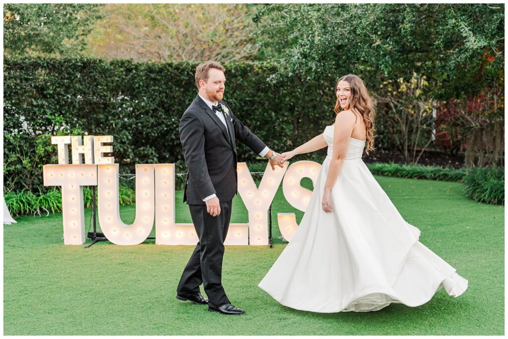 bride and groom twirling in front of their light up letters sign outside at the venue