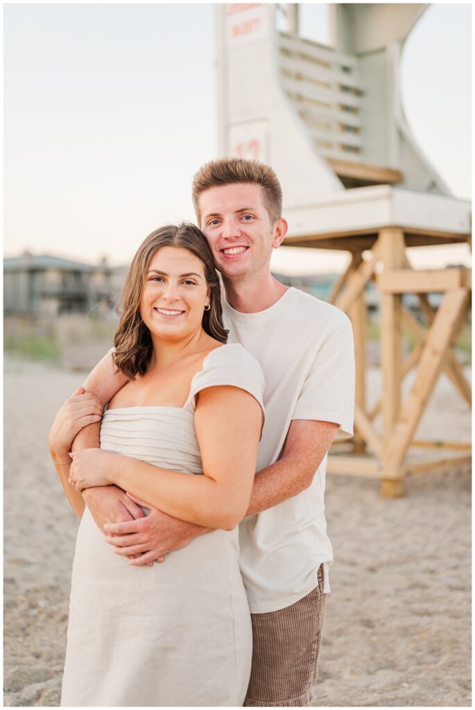 couple hugging each other in front of the lifeguard stand at Wrightsville Beach in Wilmington
