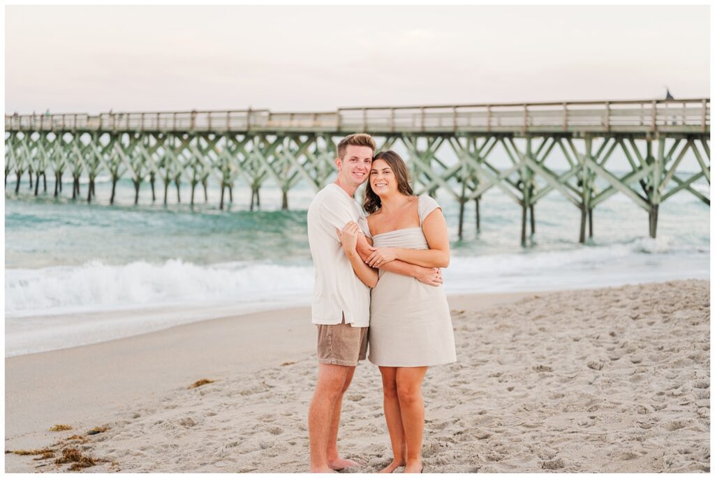 couple posing on the sand in front of the Oceania pier in Wilmington