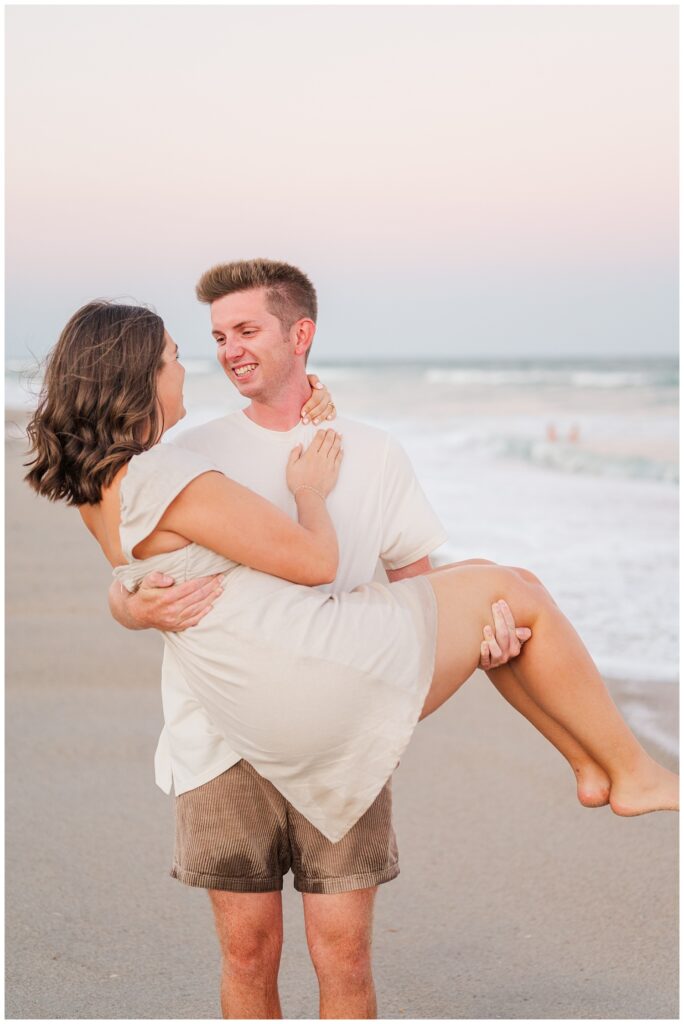 man carrying his fiancee on the beach at sunset in Wilmington